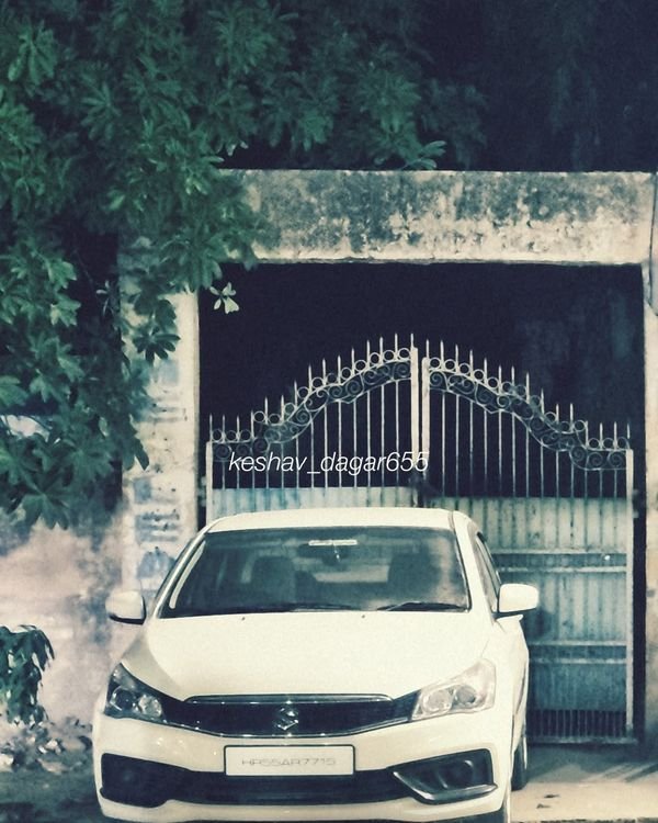 White Maruti Suzuki sedan parked at night in front of an iron gate